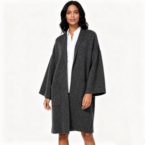 May include: A charcoal gray, open-front cardigan with large front pockets. The long-sleeved cardigan is worn over a white collared shirt. The cardigan is made of a soft, textured material.