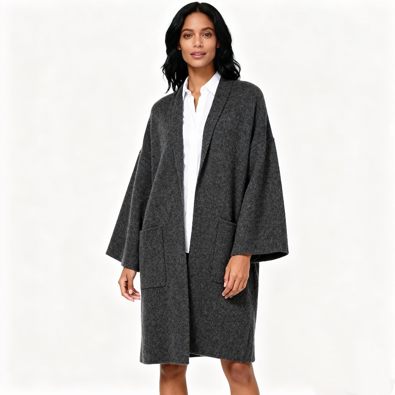 May include: A charcoal gray, open-front cardigan with large front pockets. The long-sleeved cardigan is worn over a white collared shirt. The cardigan is made of a soft, textured material.