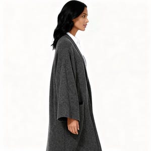 May include: A charcoal gray, longline cardigan with two front pockets. The open-front design features a relaxed fit and a soft, textured fabric. The cardigan is worn over a white collared shirt.