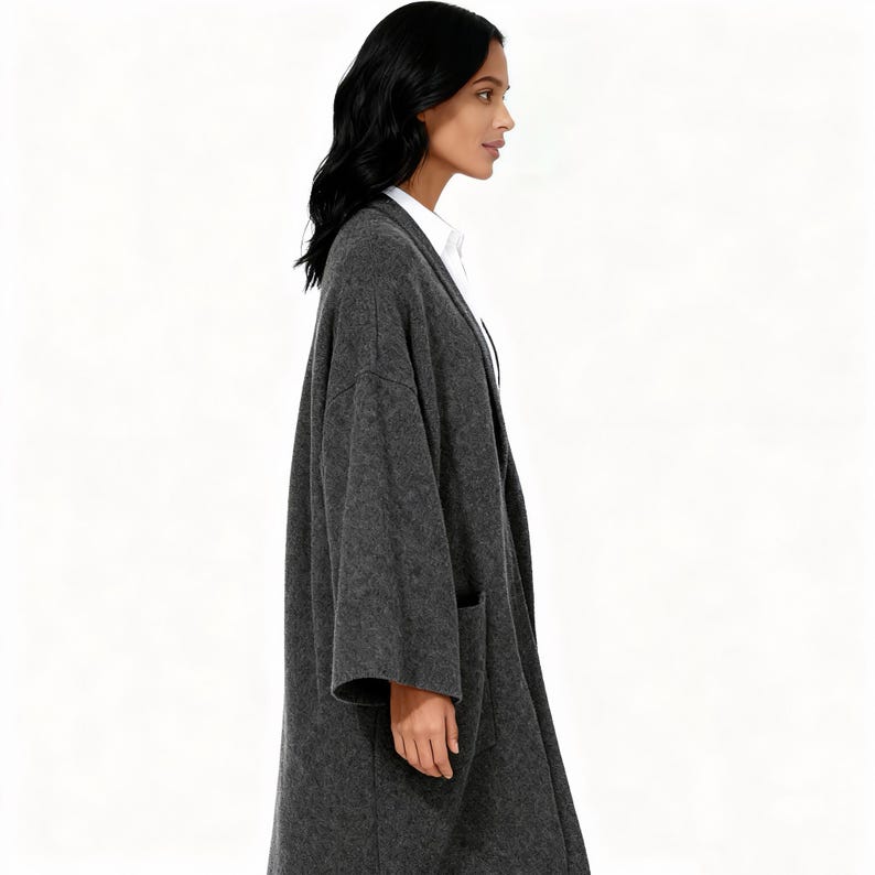 May include: A charcoal gray, longline cardigan with two front pockets. The open-front design features a relaxed fit and a soft, textured fabric. The cardigan is worn over a white collared shirt.