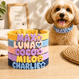 May include: A stack of five silicone dog collars in yellow, light blue, pink, purple, and dark blue. Each collar features raised, colorful letters spelling out the names MAX, LUNA, COCO, MILO, and CHARLIE, along with small decorative charms.