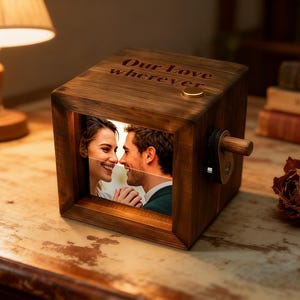 Op de afbeelding: Een houten fotoblok met een foto van een stel, van binnenuit verlicht. De bovenkant van de kubus is gegraveerd met de woorden "Our Love wherever". Een kleine messing knop en een houten slinger zijn zichtbaar.