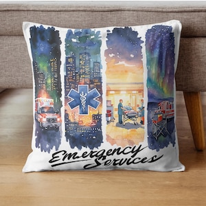 Op de afbeelding: Wit sierkussen met een aquarelontwerp met een ambulance, skyline, medisch symbool en ziekenhuisscène. Het kussen heeft de tekst "Emergency Services" in een scriptlettertype.