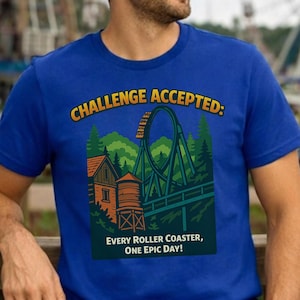 Op de afbeelding: Koningsblauw t-shirt met een afbeelding van een achtbaan, bomen en een gebouw. De tekst "CHALLENGE ACCEPTED: EVERY ROLLER COASTER, ONE EPIC DAY!" is gedrukt in geel en wit.