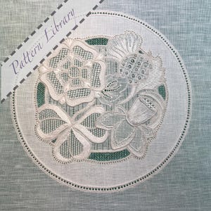 May include: A white, intricately embroidered doily with floral designs, including a rose, a flower with a seed pod, and a bow-shaped element. The doily is circular, with a green background and a dotted border. The text "Pattern Library" is visible.