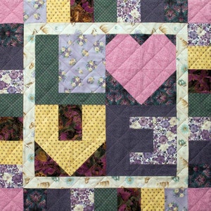 May include: A patchwork quilt featuring a pink heart, yellow polka dots, purple floral patterns, and green squares. The quilt is made from various fabrics and has a quilted texture.