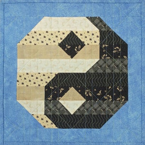 Könnte beinhalten: Ein blauer Stoffquadrat mit einem geometrischen Muster in der Mitte. Das Muster besteht aus schwarzen, weißen und beigen Stoffstücken. Das Muster ist eine Variation eines traditionellen Quiltblocks.