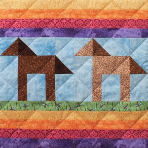 May include: A quilt with a patchwork design featuring two brown stylized animal figures on a blue background. The quilt has a multi-coloured striped border with a repeating pattern.