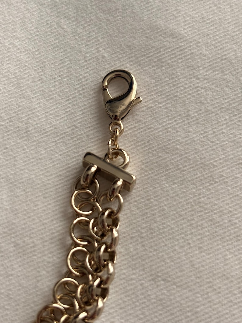 May include: A gold-toned metal chain bracelet featuring a multi-strand design composed of interlocking circular links. The bracelet is secured with a polished lobster claw clasp attached to a rectangular metal bar connector at the end of the chain.