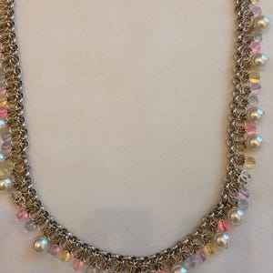 May include: A gold-tone chain necklace featuring multiple interlocking links adorned with dangling white faux pearls and translucent pink, yellow, and blue beads. Small silver-tone CC logo charms are interspersed throughout the chain design.