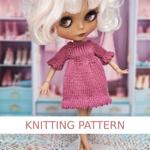 Puede incluir: Una muñeca de tez clara y cabello rubio rizado, vestida con un vestido de punto rosa con mangas cortas y un dobladillo con volantes. El texto "KNITTING PATTERN" se muestra en una pancarta blanca debajo.