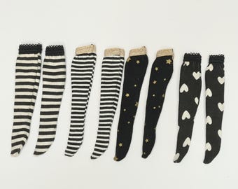 May include: A selection of knee-high socks with different designs. The socks display black and white stripes, gold stars on black, and white hearts on black. The sock tops have decorative trim.