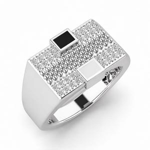 Peut inclure: Une bague en argent avec une face rectangulaire. La face est orn&eacute;e de petites perles rondes argent&eacute;es et de pierres pr&eacute;cieuses rondes et transparentes. Deux incrustations carr&eacute;es, une noire et une blanche, sont serties dans la face.