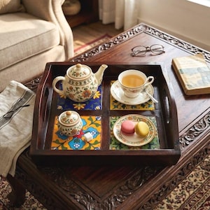 Könnte beinhalten: Ein Serviertablett aus dunklem Holz mit vier eingelegten Keramikfliesen mit bunten Blumenmustern. Das Tablett enthält eine Keramikteekanne, eine passende Zuckerdose, eine Teetasse auf einer Untertasse und einen Teller mit zwei Macarons.