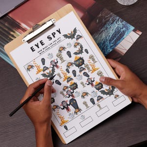 May include: A Halloween-themed "Eye Spy" game on a wooden clipboard. The game features illustrations of bats, spiders, ghosts, and other spooky characters. The title "EYE SPY" is printed at the top, with space to write answers at the bottom.