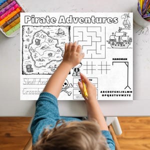 May include: A black and white activity placemat with the words "Pirate Adventures" at the top. The placemat features a treasure map, a maze, a pirate ship, and a hangman game. A child is using a yellow crayon to color the placemat.