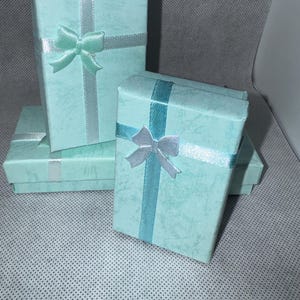 Pode incluir: Várias caixas de presente azul claro com superfícies texturizadas são dispostas em grupo. Cada caixa é adornada com uma fita e um laço em tons de azul e prata. As caixas são de tamanhos variados, sugerindo um conjunto de presentes.