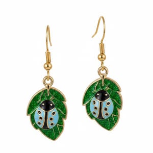 Peut inclure: Une paire de boucles d'oreilles pendantes dorées avec une breloque en forme de feuille verte scintillante et une coccinelle bleu clair et noire. Les boucles d'oreilles sont suspendues à des crochets dorés, avec un motif d'insecte détaillé.