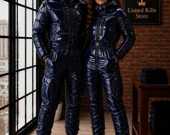 May include: Two individuals wearing matching navy blue, high-gloss, patent-finish, hooded jumpsuits with front zippers, belted waists, and side cargo pockets. The jumpsuits feature a quilted texture and are paired with black boots and sunglasses.
