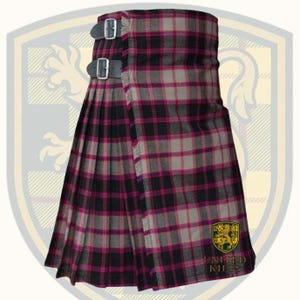Puede incluir: Un kilt tradicional con un patr&oacute;n de cuadros en tonos negro, gris y magenta. El kilt tiene dos correas de cuero con hebillas plateadas y est&aacute; plisado. En la esquina inferior derecha se muestra un emblema dorado y verde con el texto "UNITED KILTS".