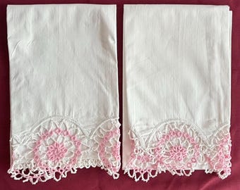 May include: Two white pillowcases with pink crocheted lace trim. The lace has a delicate floral pattern.