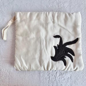 May include: A white pillow with a black embroidered design. The design is a stylized floral pattern.