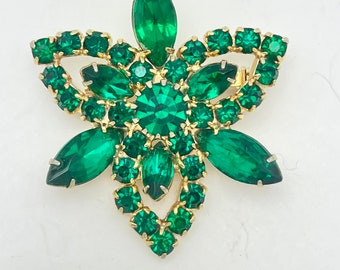 Pode incluir: Broche vintage com design floral. O broche apresenta uma moldura de metal dourado e é adornado com strass verde esmeralda em várias formas, incluindo cortes marquesa e redondos. O broche tem um fecho de alfinete na parte de trás.