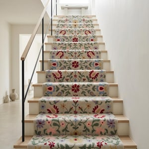 May include: A staircase runner featuring a light beige background with a repeating floral pattern in shades of red, pink, blue, yellow, and green. The carpet covers each step, showcasing symmetrical botanical motifs with leaves and blossoms.