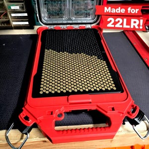 May include: A red case with a black interior grid filled with small, gold-colored objects. The case has a handle and metal loops. Text on a red banner reads "Made for 22LR!"