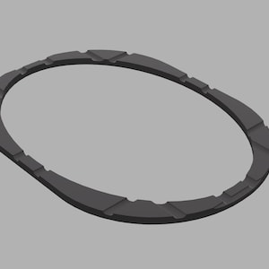 May include: A dark gray, oval-shaped object with a textured surface. The object has a series of rectangular cutouts along its outer edge. The design is simple and geometric, with a modern aesthetic.
