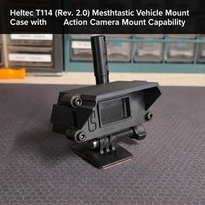 May include: Black Heltec T114 (Rev. 2.0) Mesthtastic Vehicle Mount Case with Action Camera Mount Capability. The mount has a rectangular frame with a small screen and a cylindrical extension. It is mounted on a black base.
