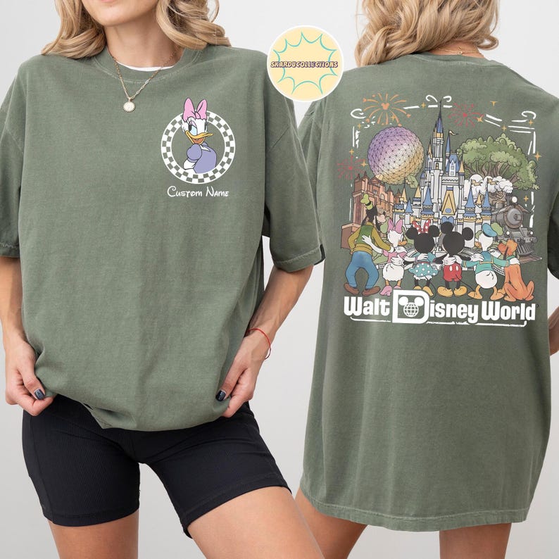 May include: Olive green t-shirt with a Daisy Duck graphic on the front, set within a checkered circle. The back showcases a colourful illustration of Walt Disney World characters and landmarks, with the words "Walt Disney World".