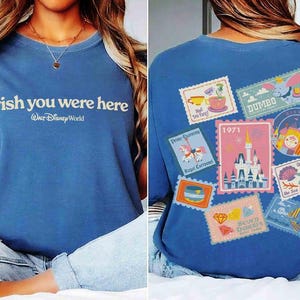 May include: Blue t-shirt with the text "wish you were here" and "Walt Disney World". The back of the shirt features various Disney-themed postage stamp designs, including Dumbo and a castle, with the year 1971.