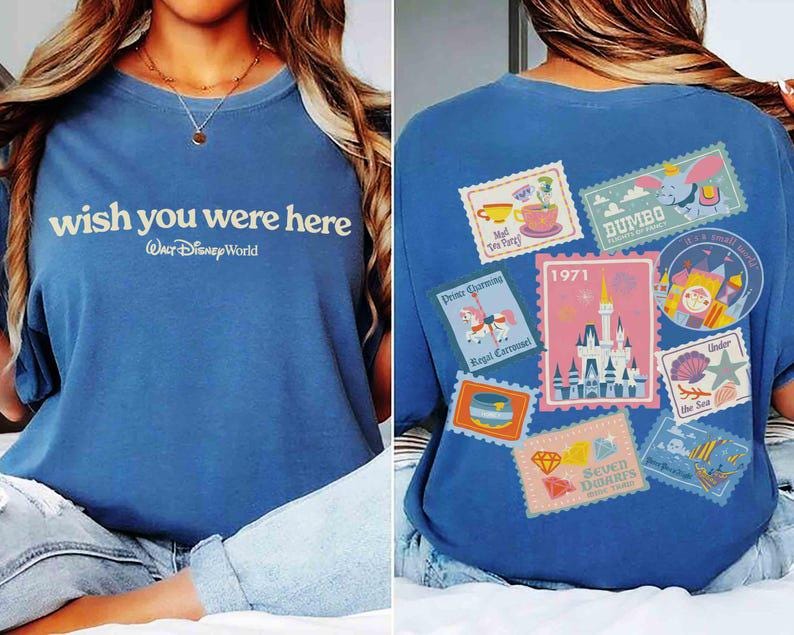May include: Blue t-shirt with the text "wish you were here" and "Walt Disney World". The back of the shirt features various Disney-themed postage stamp designs, including Dumbo and a castle, with the year 1971.