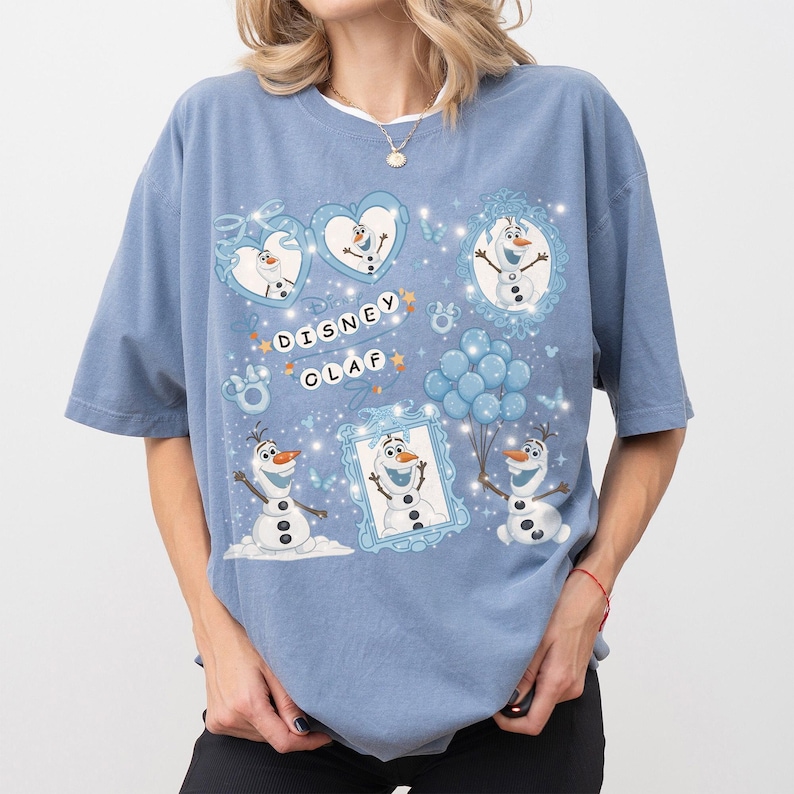 May include: A light blue t-shirt featuring a Disney Olaf graphic. The design includes multiple images of Olaf, the snowman character, within frames and hearts, along with the text "Disney Olaf". The shirt has short sleeves and a relaxed fit.