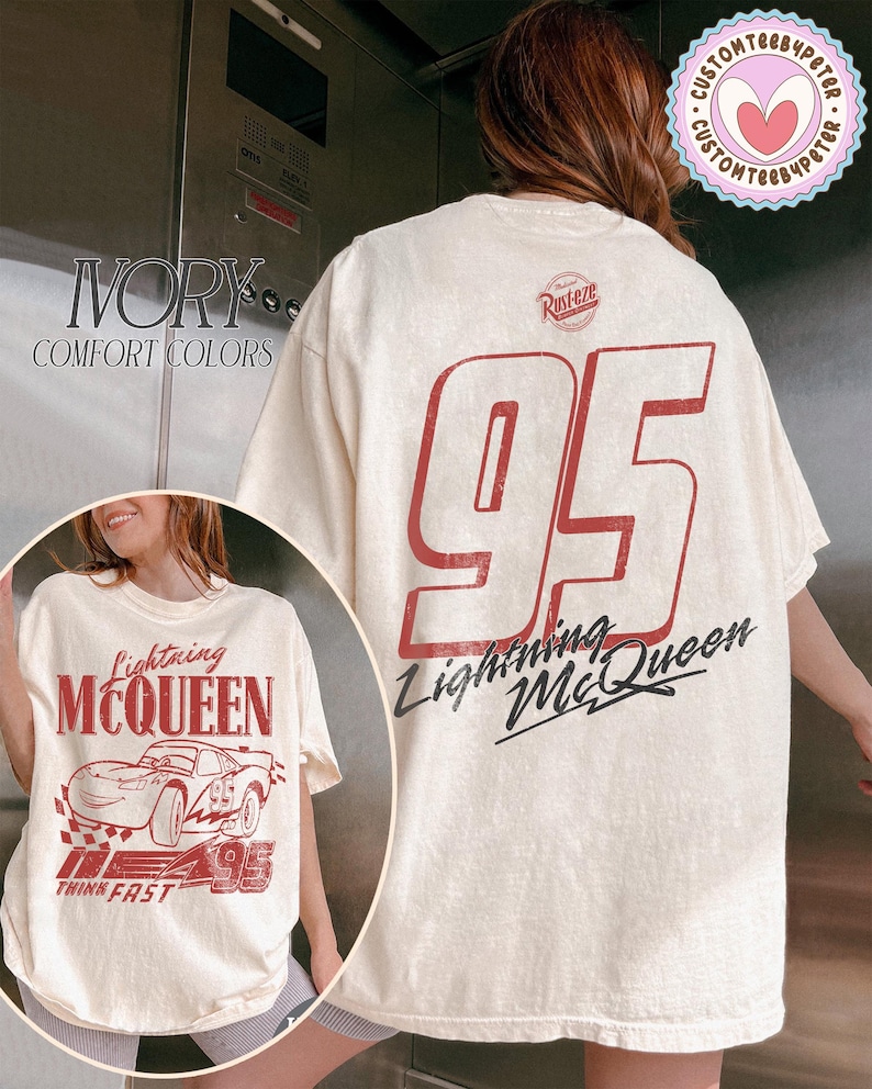 May include: Ivory-colored Lightning McQueen t-shirt. The front features a graphic of the character and the text "Lightning McQueen" and "95". The back displays a large "95" and "Lightning McQueen" in red and black.