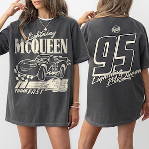 May include: Dark gray Lightning McQueen graphic t-shirt. The front features a stylized image of the race car with the text "Lightning McQueen", "95", and "Think Fast". The back of the shirt displays a large "95" and "Lightning McQueen" text.