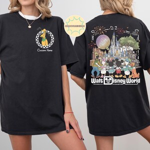 May include: Black t-shirt with a Pluto graphic in a chequered circle on the front. The back shows a colourful graphic of Disney characters and the text "Walt Disney World". The shirt has a crew neck and short sleeves.