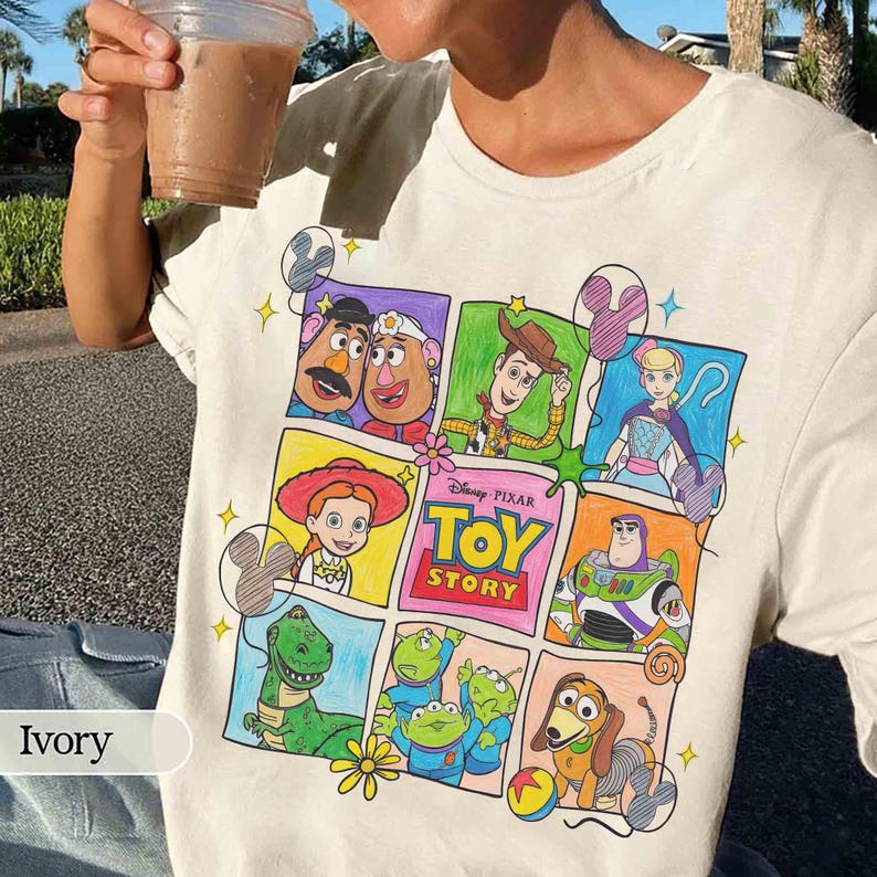 May include: Ivory t-shirt with a colourful grid design featuring characters from the Toy Story film. The graphic includes Woody, Buzz Lightyear, and other characters from the Disney Pixar movie.