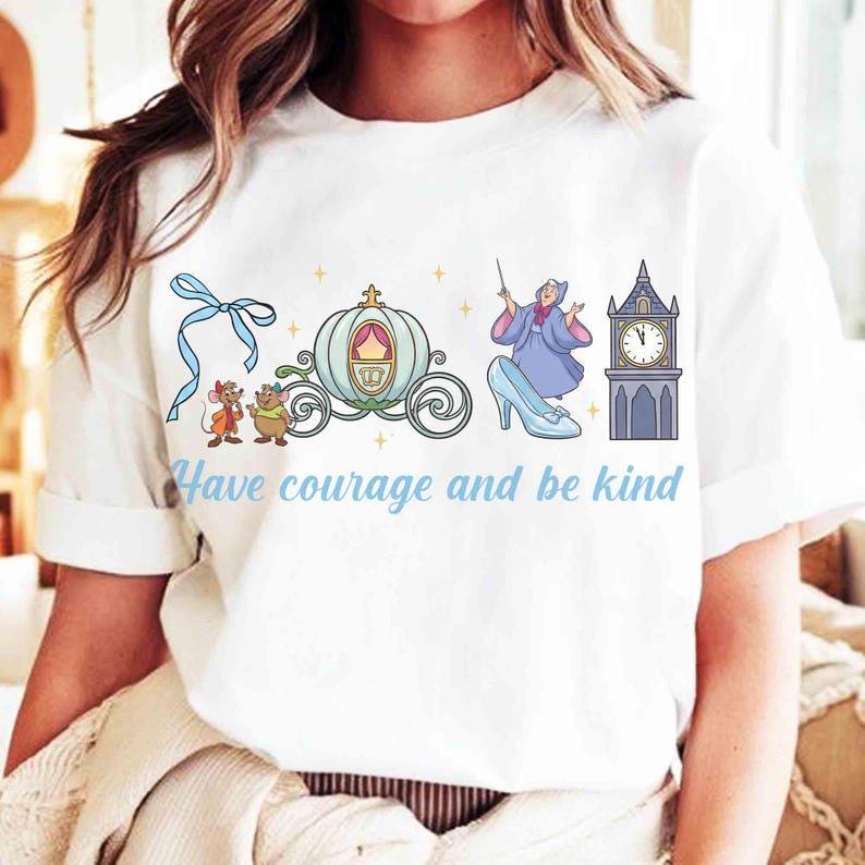 Peut inclure: T-shirt blanc avec une illustration sur le th&egrave;me de Cendrillon. Le motif comprend un carrosse, une tour d'horloge, une f&eacute;e marraine, des souris et le texte "Have courage and be kind" en bleu clair.