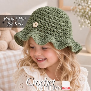 May include: A sage green crocheted bucket hat for kids featuring a small white flower embellishment on the front. The text Bucket Hat for Kids and Crochet PATTERN PDF is visible on the image. The hat has a wide, wavy brim and textured stitches.