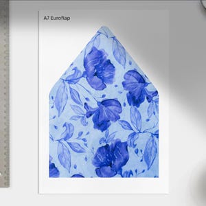 May include: A7 Euroflap envelope with a watercolor floral design. The envelope features a light blue background with large, deep blue flowers and leaves. A metal ruler is on the left side of the image.