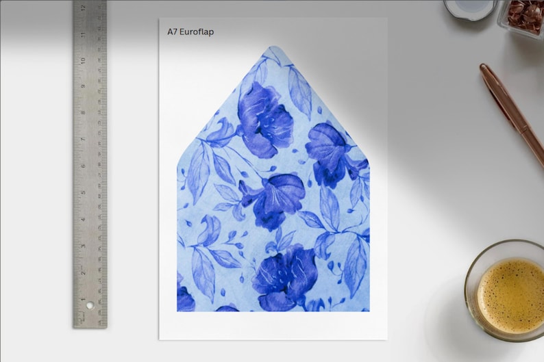 May include: A7 Euroflap envelope with a watercolor floral design. The envelope features a light blue background with large, deep blue flowers and leaves. A metal ruler is on the left side of the image.