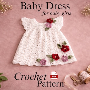 Puede incluir: Vestido de bebé blanco de ganchillo con detalles de flores rojas y moradas. El vestido se muestra sobre una superficie rosa con el texto "Baby Dress for baby girls" y "Crochet Pattern". Flores decorativas y materiales de manualidades rodean el vestido.