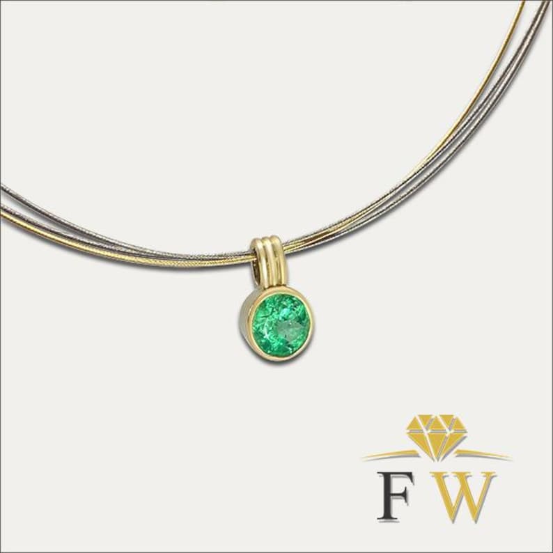 May include: A necklace featuring a round, faceted green gemstone set in a yellow gold bezel pendant. The pendant hangs from a multi-strand chain composed of thin, flexible gold and silver-toned wires. A logo with the letters FW is visible.