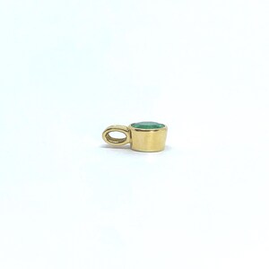 May include: A gold pendant featuring a round, bezel-set green gemstone. The pendant has a smooth, polished gold finish and a small, integrated circular bail at the side for attachment to a chain, showcasing a simple and clean design.