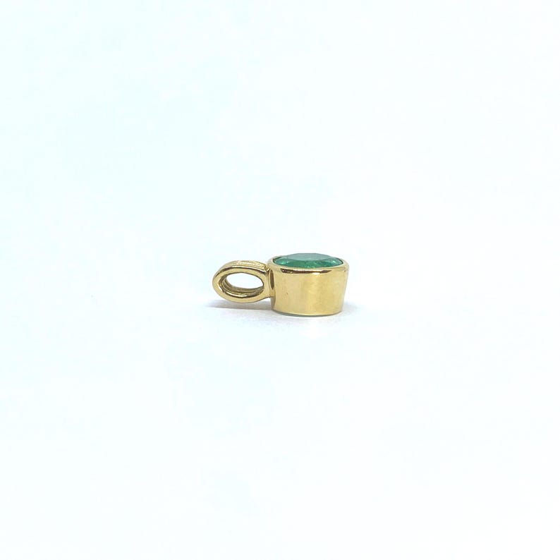 May include: A gold pendant featuring a round, bezel-set green gemstone. The pendant has a smooth, polished gold finish and a small, integrated circular bail at the side for attachment to a chain, showcasing a simple and clean design.