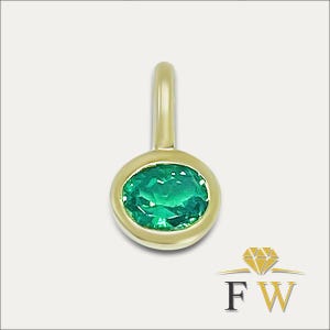 May include: A gold pendant featuring a single oval-cut green emerald gemstone set in a smooth bezel setting. The pendant includes a polished gold bail at the top for attachment to a chain. The design is simple, highlighting the vibrant green stone.