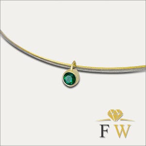 May include: A necklace featuring a thin, two-toned silver and gold wire collar. A single, round, faceted green gemstone is set in a gold bezel pendant that hangs from the wire. The logo FW with a diamond icon is visible in the bottom right corner.