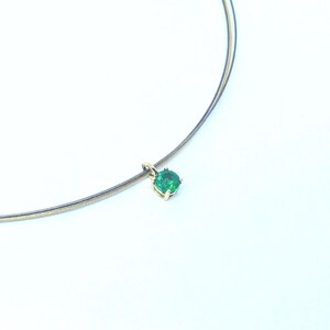 May include: A delicate necklace featuring a vibrant green gemstone pendant. The pendant is set in a gold-colored metal and hangs from a thin, multi-strand chain. The gemstone is round and appears to be emerald. The necklace is displayed against a white background.